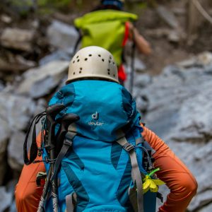 Two hikers with backpacks and helmets navigating a rocky trail in the forest.